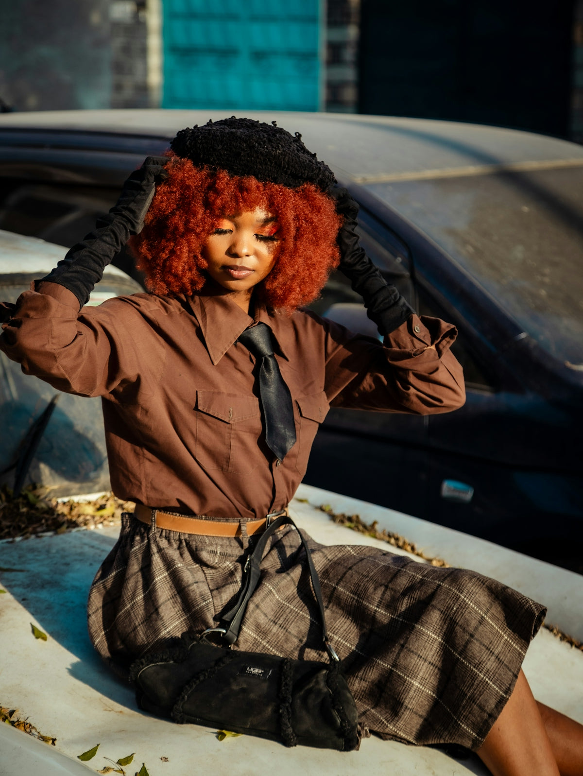 A woman with red hair sitting on the hood of a car