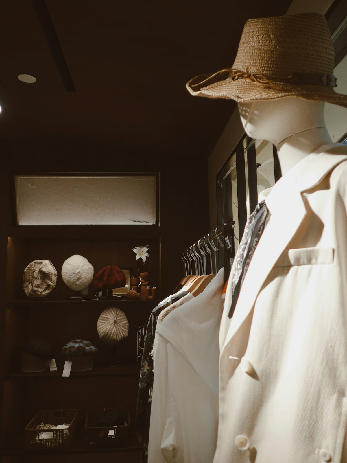 Mannequin wearing a straw hat and jacket in store.