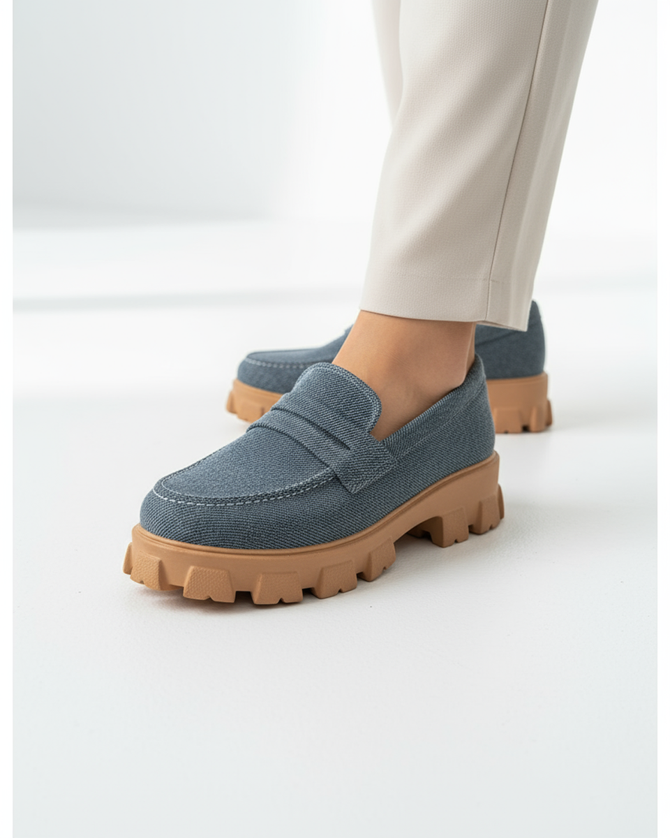 Blue loafers with brown soles worn by a person on a white background