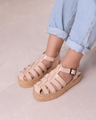 Beige sandals with woven sole worn by a person in light blue jeans on a neutral background