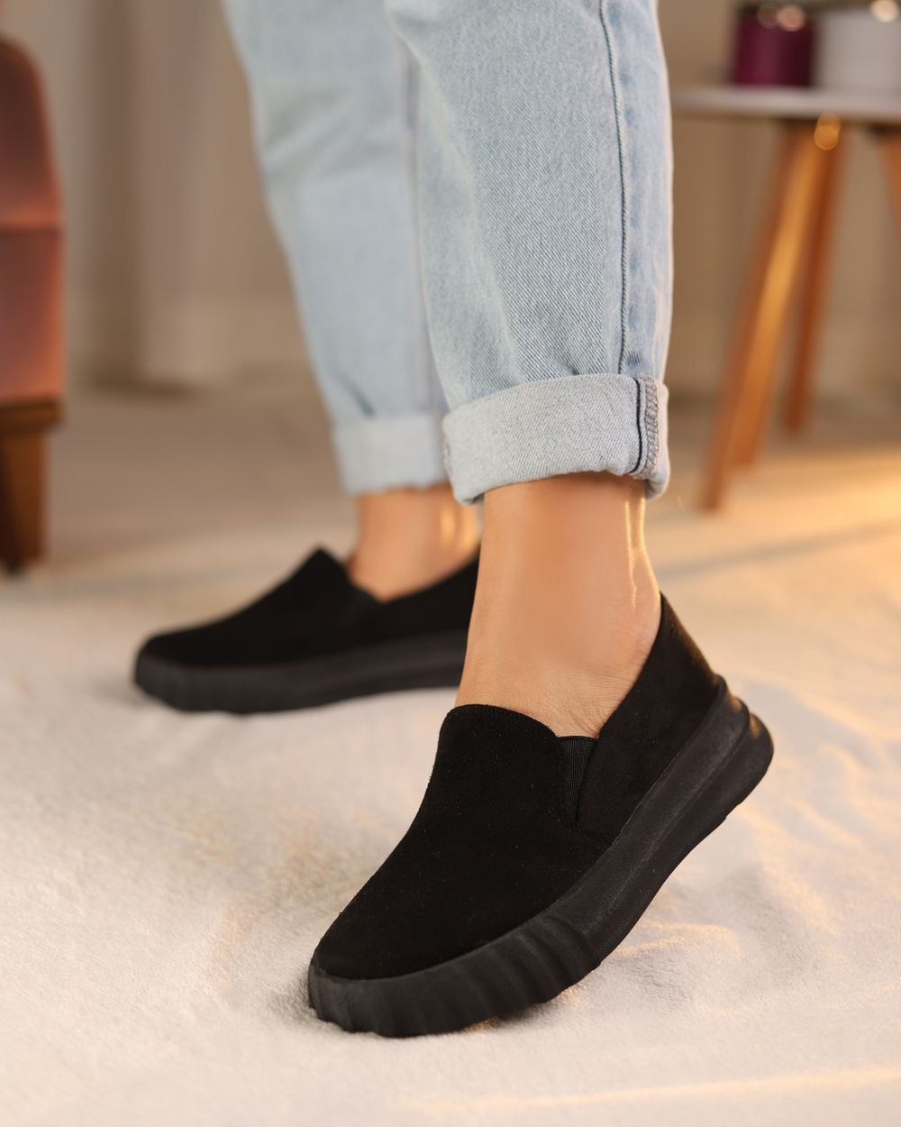 A person wearing black slip-on shoes From Hatchill with rolled-up blue jeans.