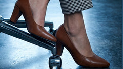 Brown high-heeled shoes worn with checkered pants on a reflective floor.