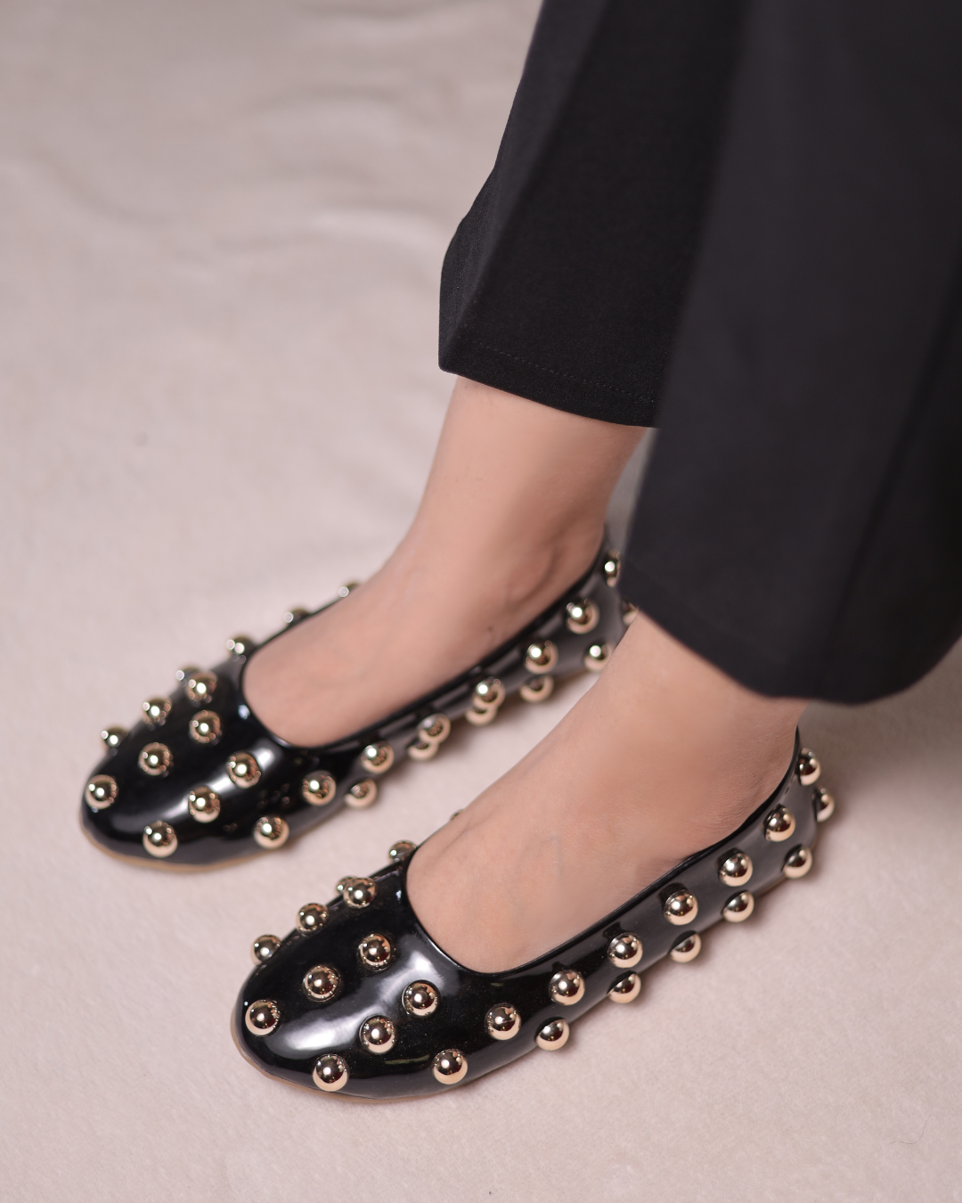 Black studded flats worn with black pants on a neutral background