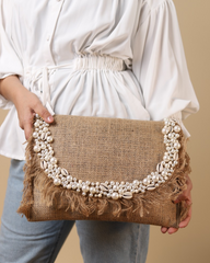 A person holding a beige clutch bag with a pearl-like texture and decorative elements resembling pearls along the edge.