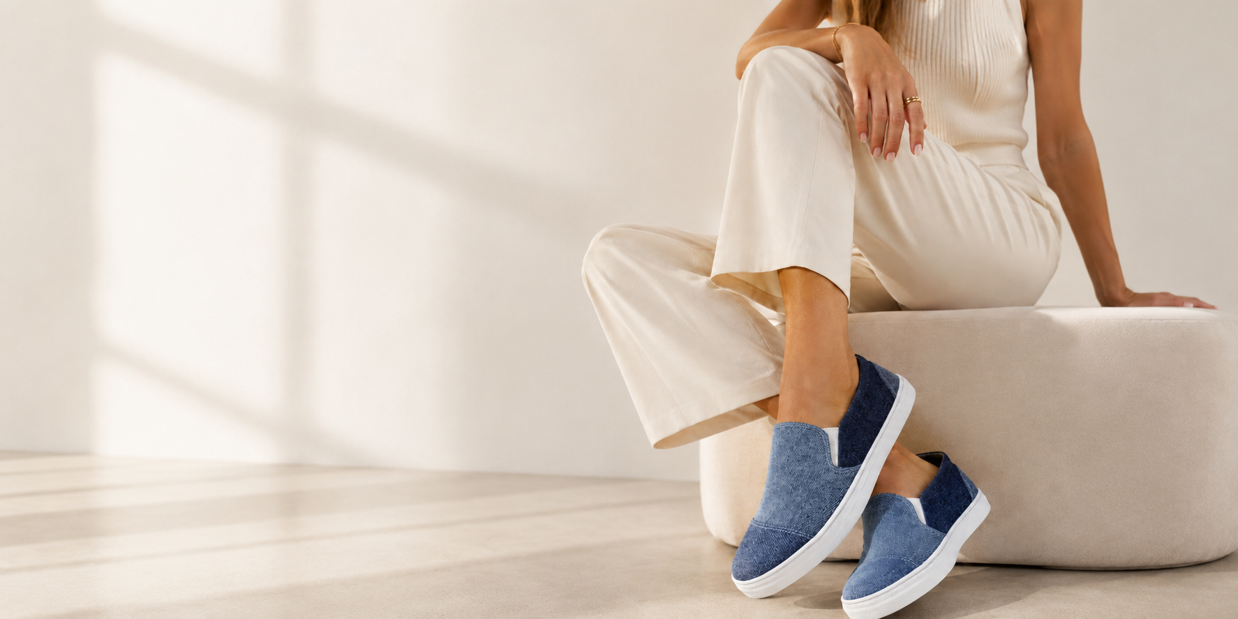 Person wearing blue slip-on shoes sitting on a white surface with a neutral background