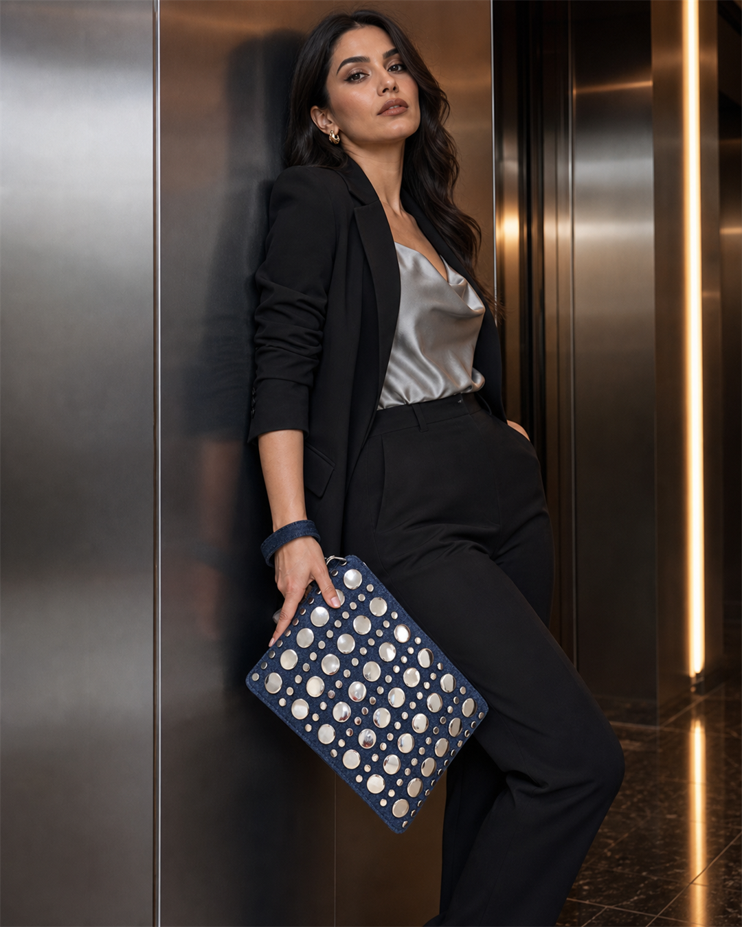 Denara studded denim clutch carried diagonally by female model in evening elevator - creative view
