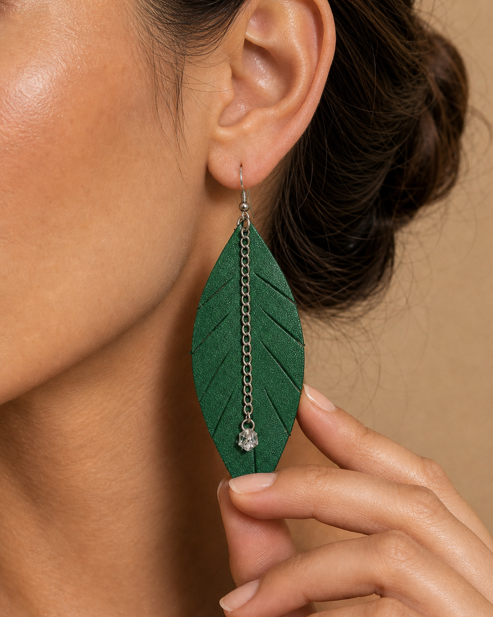 Close-up detail of green leaf earring with silver chain and crystal drop