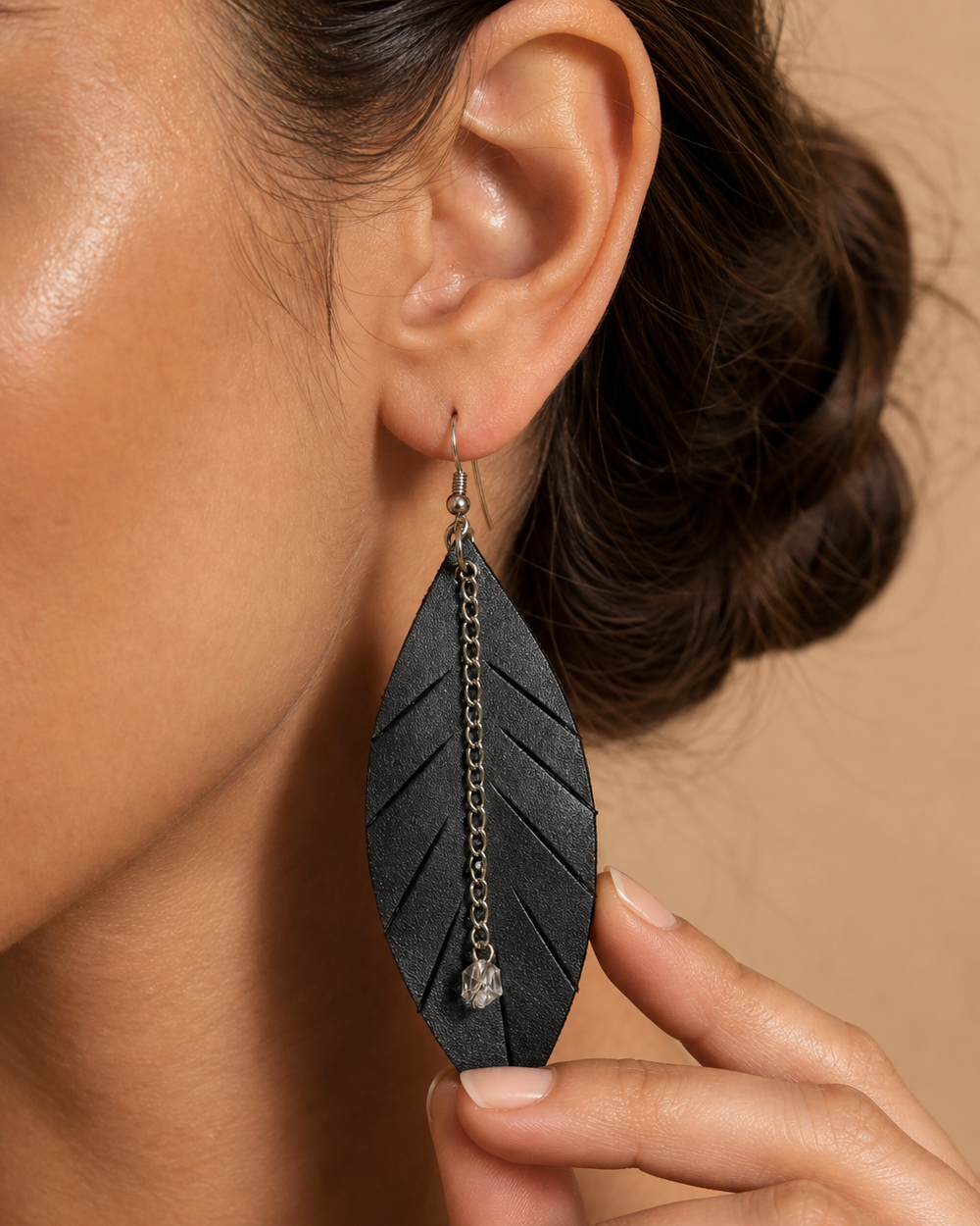 Close-up detail of black leaf earring with silver chain and crystal drop